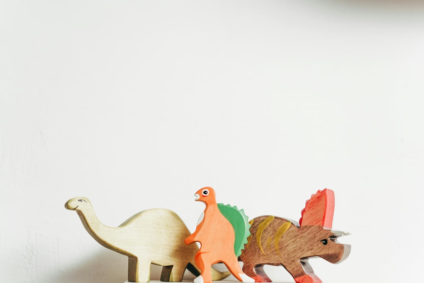Holzspielzeug-Dinosaurier in einer Reihe – Brachiosaurus, Stegosaurus und Triceratops als farbenfrohe Figuren