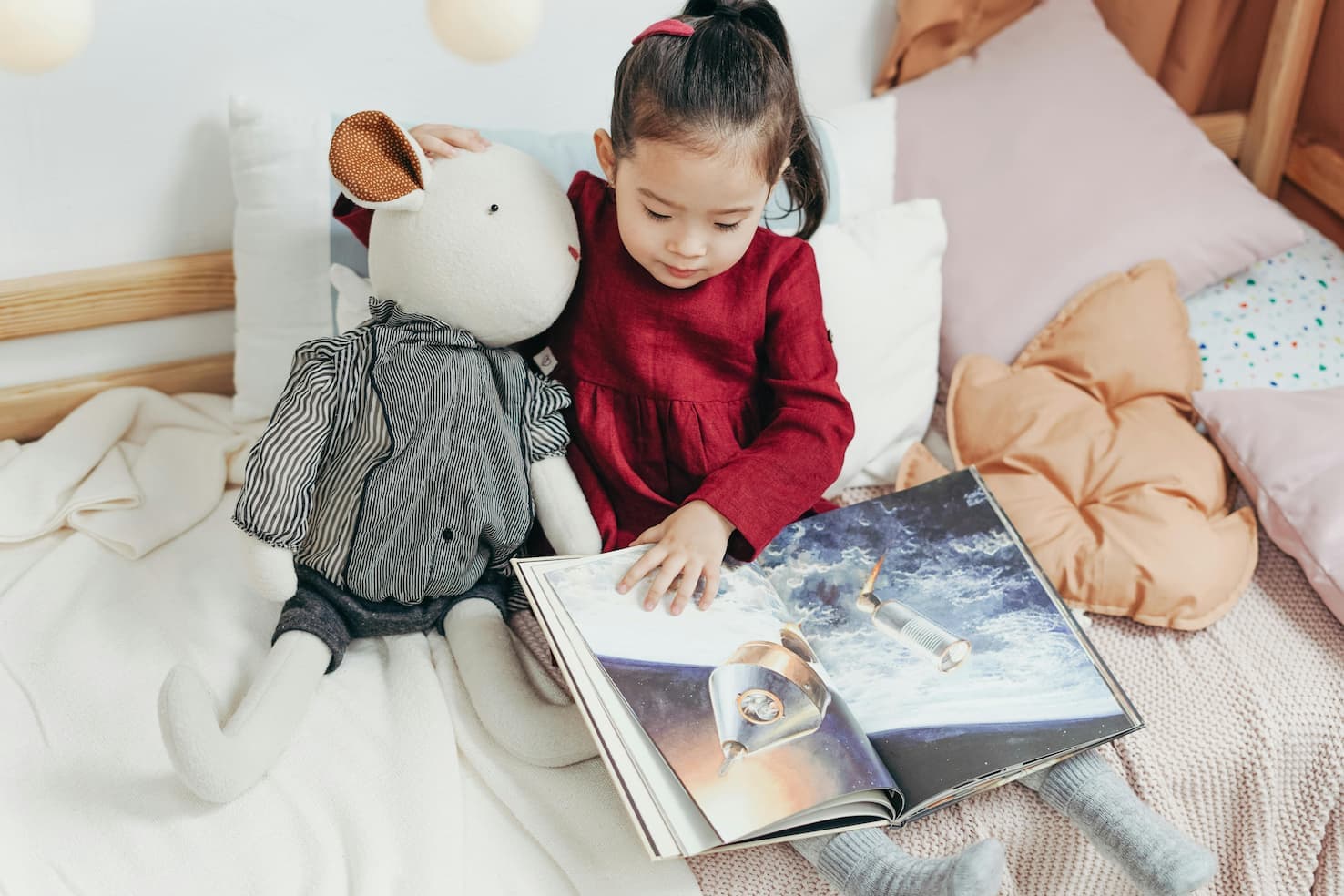 Mädchen betrachtet mit ihrer Kuscheltier-Maus ein Raumschiff-Bild im Buch – Kinderbücher ab 5 Jahren mit Abenteuern und erstem Sachwissen